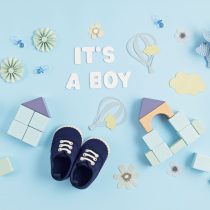 Cute newborn baby boy shoes with festive decoration over blue background. Baby shower, birthday, invitation or greeting card idea